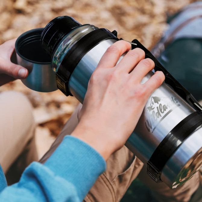 A drink bottle in silver with a black strap, being held while pouring into a cup. It features a logo.
