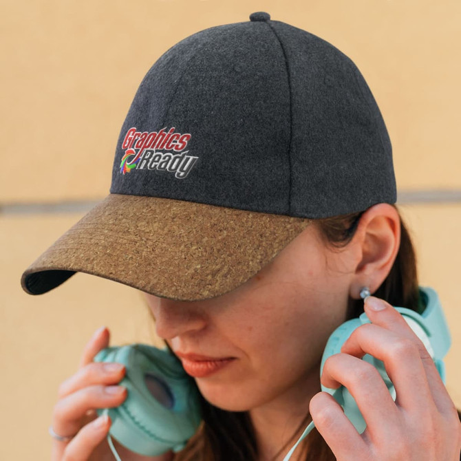 A dark grey cap with a cork brim and a logo, worn by a person holding headphones.