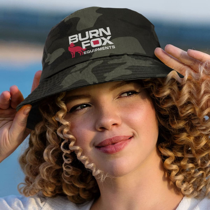 A camouflage bucket hat with a logo, featuring shades of green and black, worn by a young woman with curly hair.