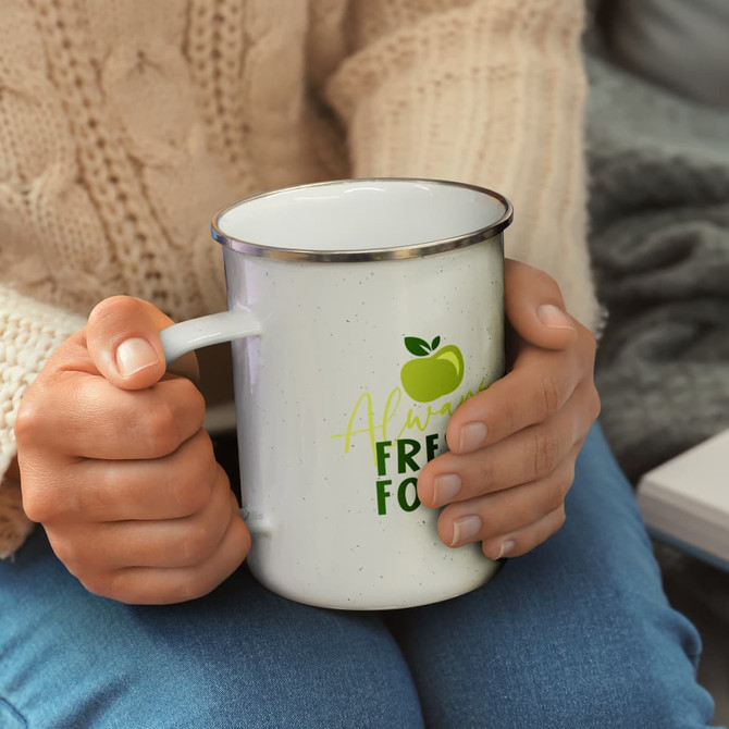 A white enamel mug with a silver rim, held by a person wearing a knitted sweater, featuring a logo.