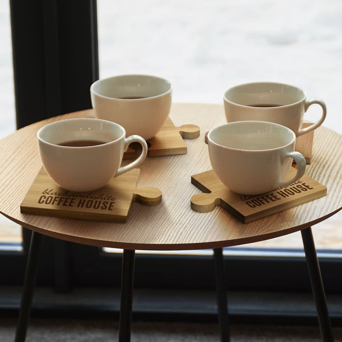 A set of four wooden coasters with puzzle piece shapes, each holding a white cup of tea or coffee.