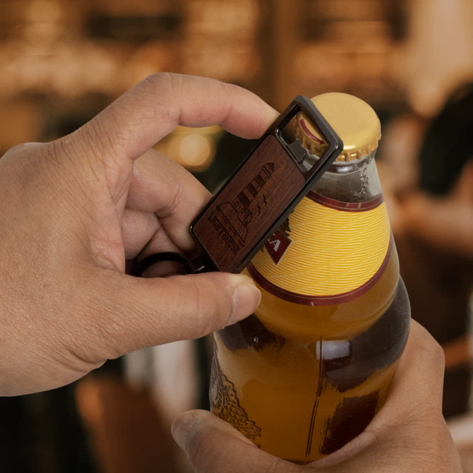 A drink bottle opener key ring with a wooden finish and a logo, held over a beer bottle.