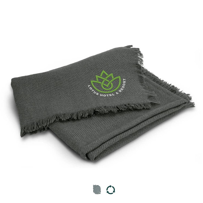 A grey herringbone throw blanket with fringed edges and a logo of a lotus flower.