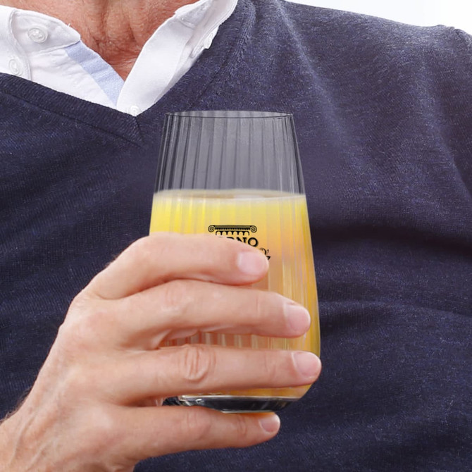 A glass tumbler with a ribbed design, partially filled with orange juice, held in a person's hand.