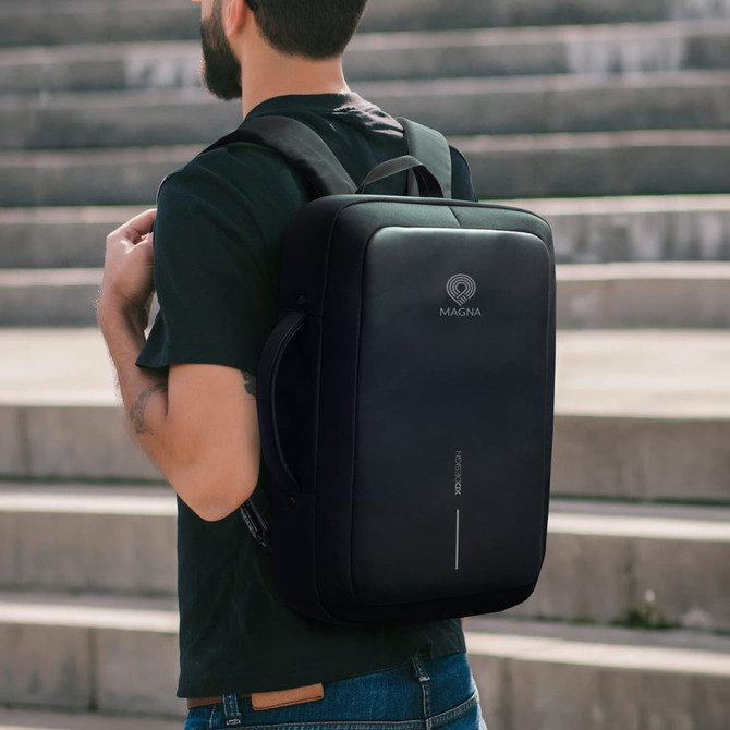A black anti-theft backpack with a sleek design, featuring a logo and a top handle, worn on a person’s back.