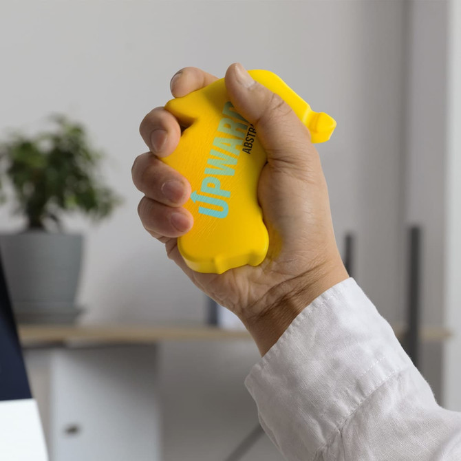 A yellow stress ball in the shape of a hand, being squeezed by a person in a white shirt.