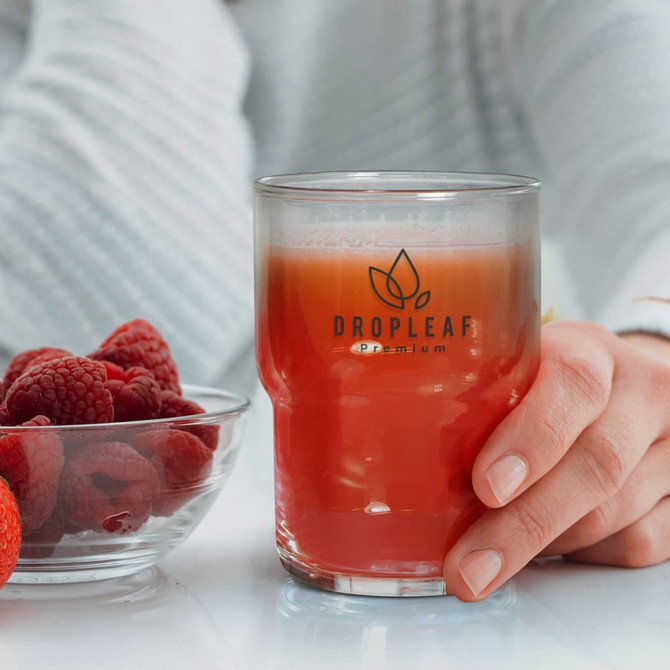 A stackable glass tumbler filled with a reddish drink, accompanied by a bowl of raspberries and strawberries.