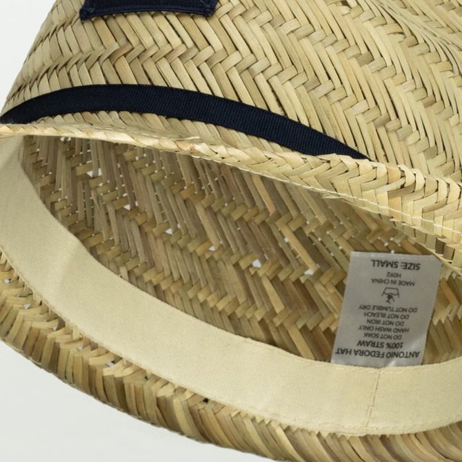 A tan straw fedora hat with a black band and a tag inside, featuring a logo.