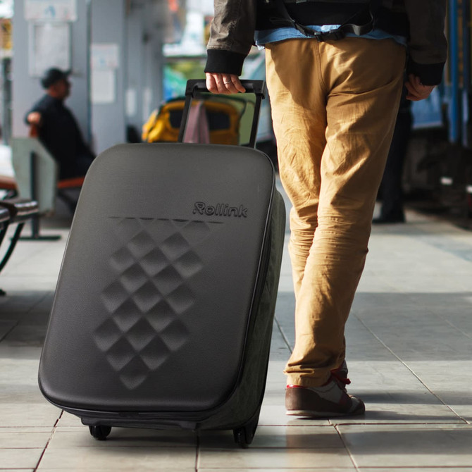 A medium black wheeled suitcase with a textured surface and a logo, being pulled by a person in beige trousers.