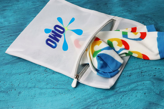 A white laundry bag with a logo, featuring colourful patterned socks peeking out from the zippered opening.