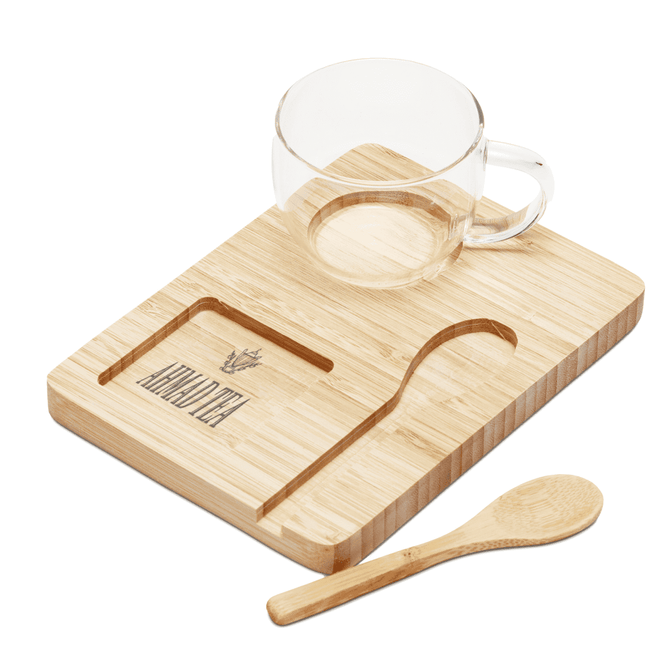 A clear glass cup, a bamboo tray with a carved groove, and a wooden spoon, all in natural tones.
