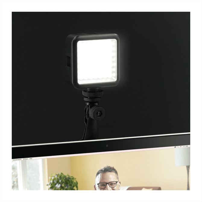 A square portable video light in black, mounted on a tripod, illuminating a computer screen.