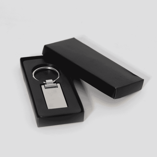 A silver keychain displayed inside a black box. The keychain has a rectangular shape with a polished finish.
