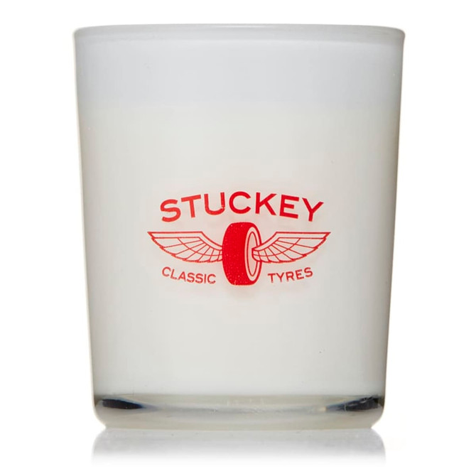 A glass candle with a white wax interior and a red logo featuring wings and a tyre motif.