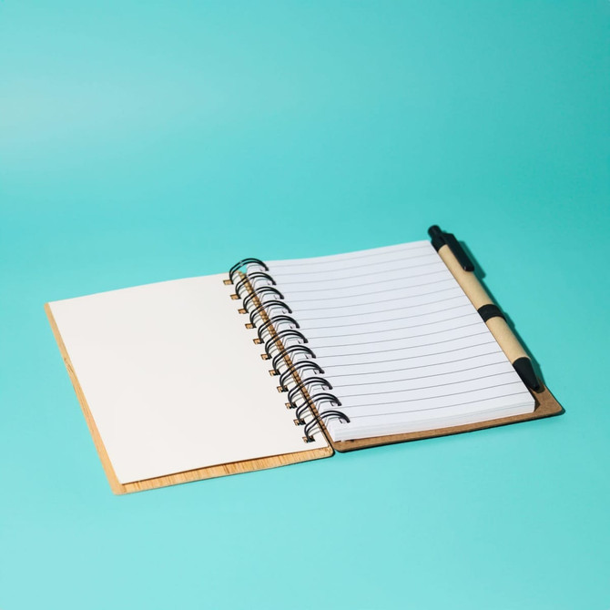 A bamboo notebook with a pen, featuring lined pages and a spiral binding, on a vibrant turquoise background.
