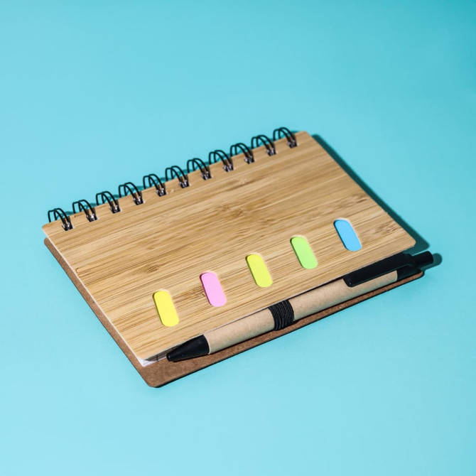 A bamboo notebook with a spiral binding, featuring colourful tabs and a matching pen, set against a blue background.