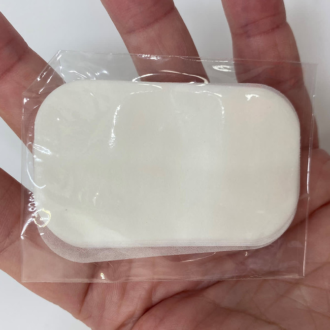 A hand holding a clear packaging containing a white, oval-shaped product. The product has a soft texture.