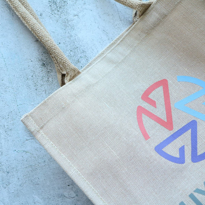 A beige jute tote bag with a colourful logo and sturdy woven handles.