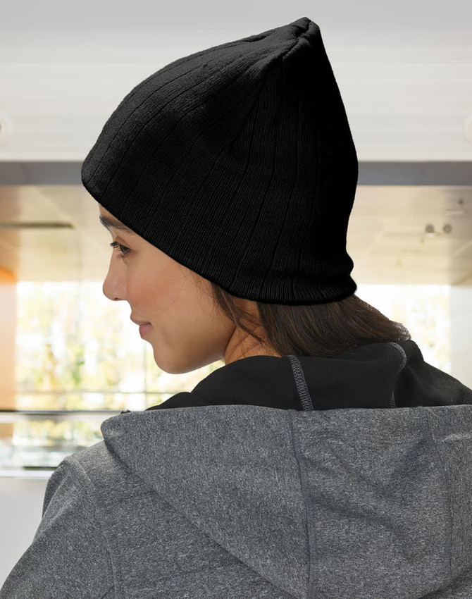 A beige cable knit beanie with a fleece headband, worn on a person’s head, seen from the side.