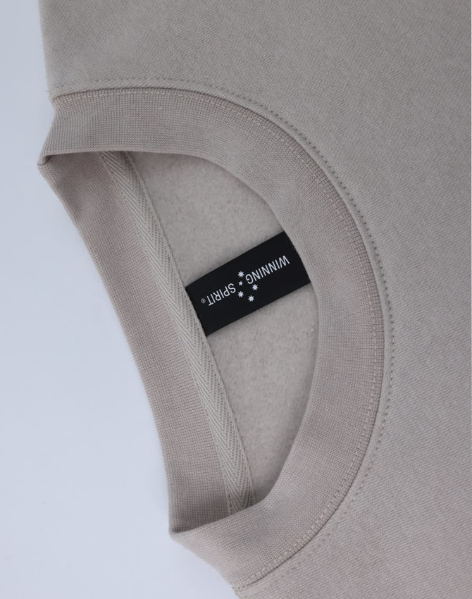 A crew neck sweater in a light beige colour, featuring a label and a soft fleecy texture.