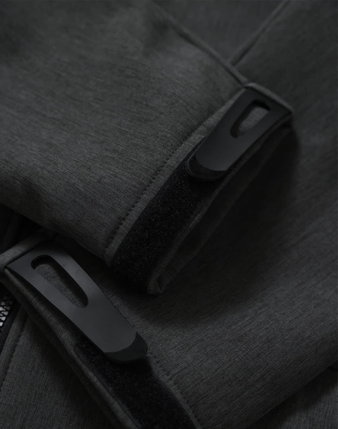 A close-up of grey softshell fabric featuring black fasteners and cuffs on a full zip hoodie. It includes a branding logo.