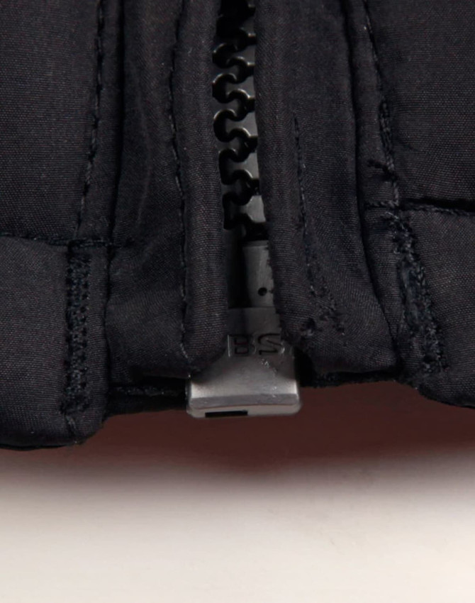 A close-up of a black heavy quilted jacket, highlighting the zip and stitching details. The jacket features a logo.