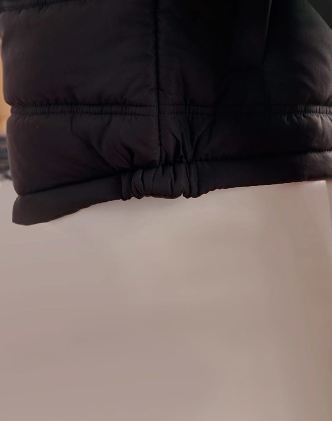 A black heavy quilted puffer jacket featuring a cinched hem and a smooth fabric texture. It has a logo visible.