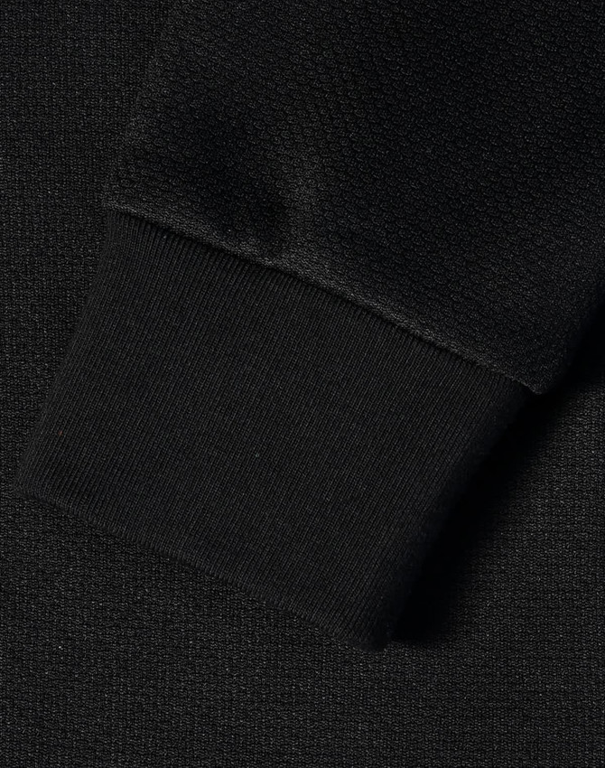 A close-up of a black jacquard fleece jacket's textured fabric and cuff. Features a logo.