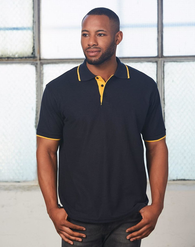 A black polo shirt with yellow detailing, featuring a collar and a logo, modeled by a man in an industrial setting.