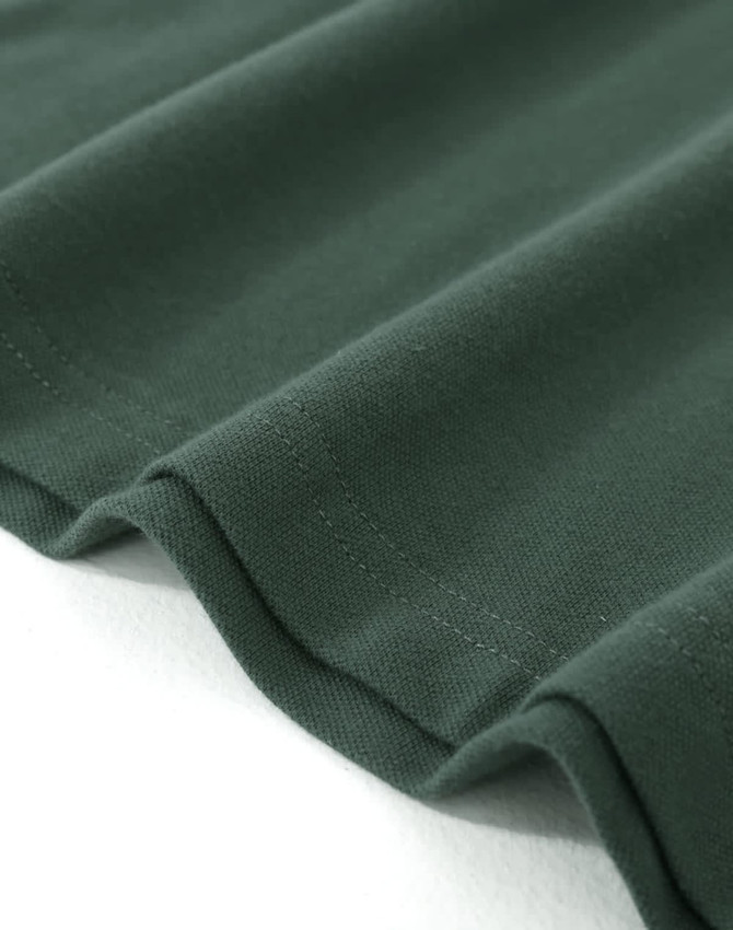 A close-up of a dark green cotton stretch polo shirt, showcasing the fabric's texture and the hem.