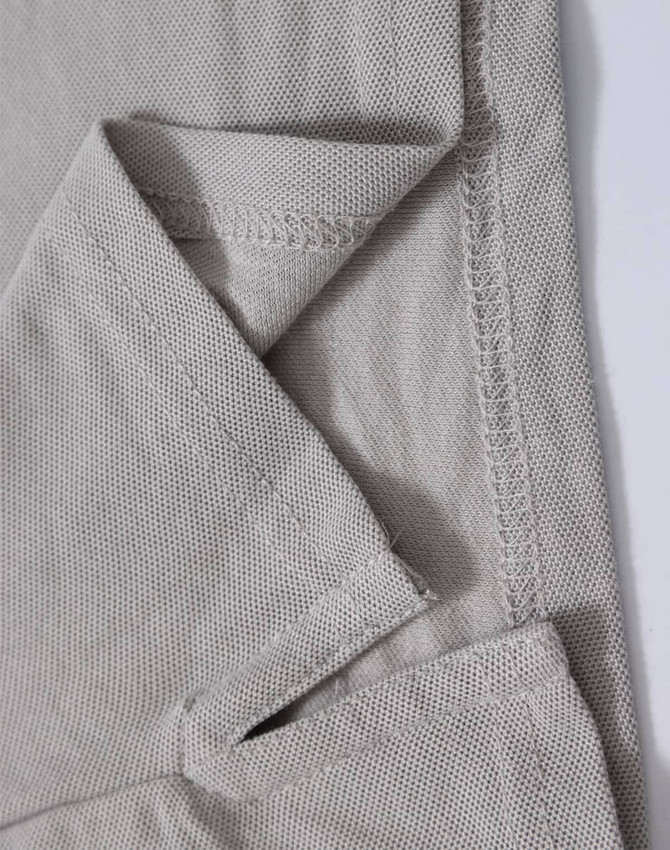 A close-up of a light grey polo shirt, showing the textured fabric and stitching details. The shirt features a logo.