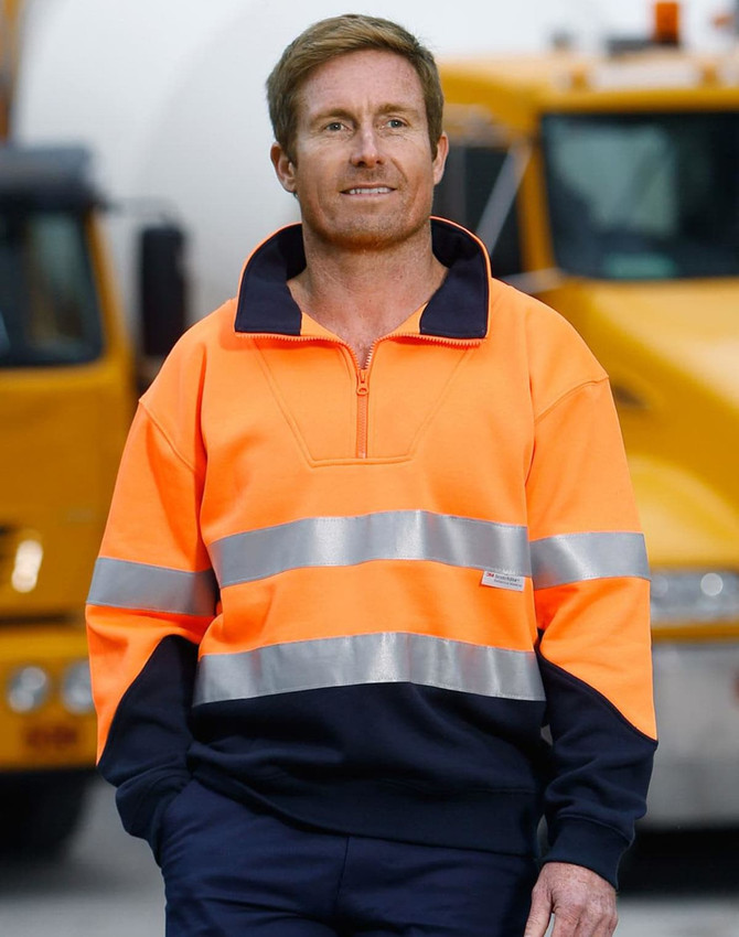 Hi-Vis long-sleeve fleece collar sweater in orange with reflective strips, paired with navy trousers. Features branding.