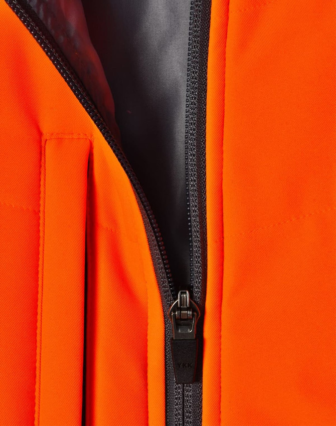 A close-up of an orange quilted safety jacket featuring a black zipper and lining. It has a logo on the fabric.