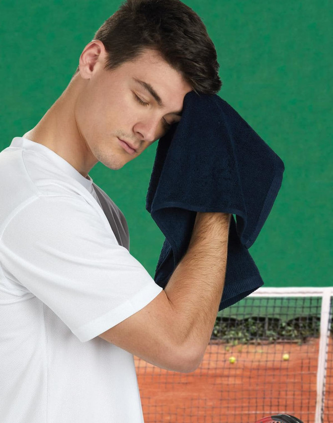 A man in a white shirt wipes his forehead with a dark navy hand towel, set against a green background.