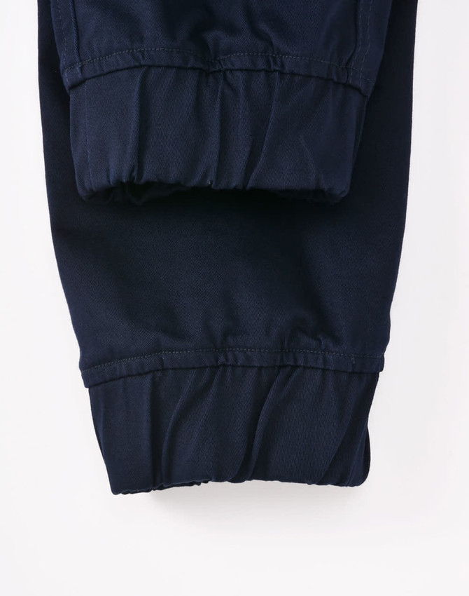 A pair of navy unisex cotton stretch drill cuffed work pants with gathered cuffs. Features a logo on the waistband.