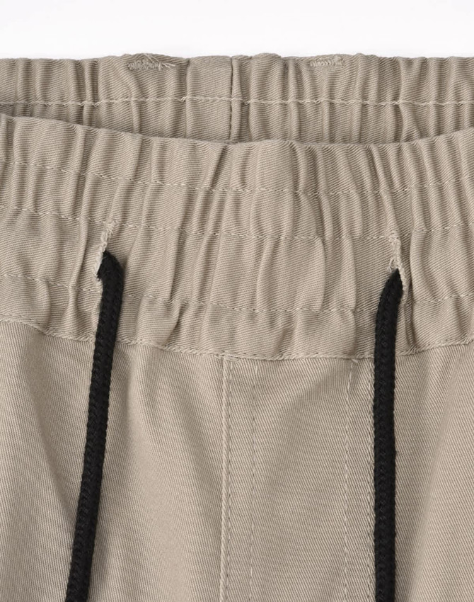 A pair of unisex cotton stretch drill cuffed work pants in a light beige colour with an elastic waistband and drawstring.