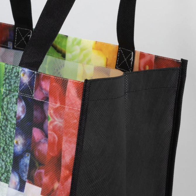 A black tote bag with a colourful, patterned interior featuring various fruits and vegetables. It has sturdy handles.