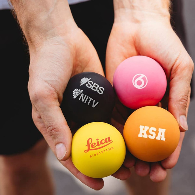 Four colourful high bounce balls in hand: black, pink, orange, and yellow, each with different logos.