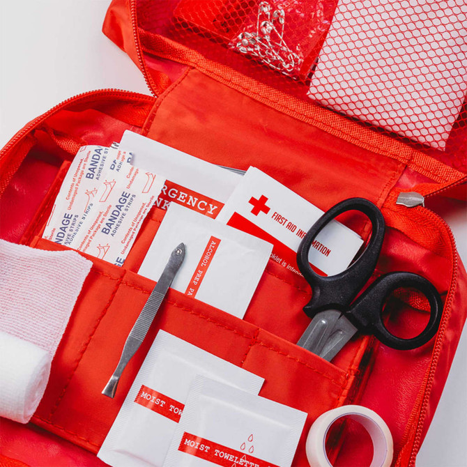 A red first aid kit containing bandages, scissors, emergency information cards, tweezers, and other medical supplies.