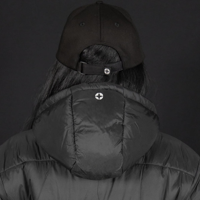 A black puffer jacket with a hood, worn by a person wearing a black cap, featuring a logo on the back.