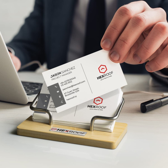 A bamboo business card stand holds several white business cards with black text, alongside a smartphone and a notebook.