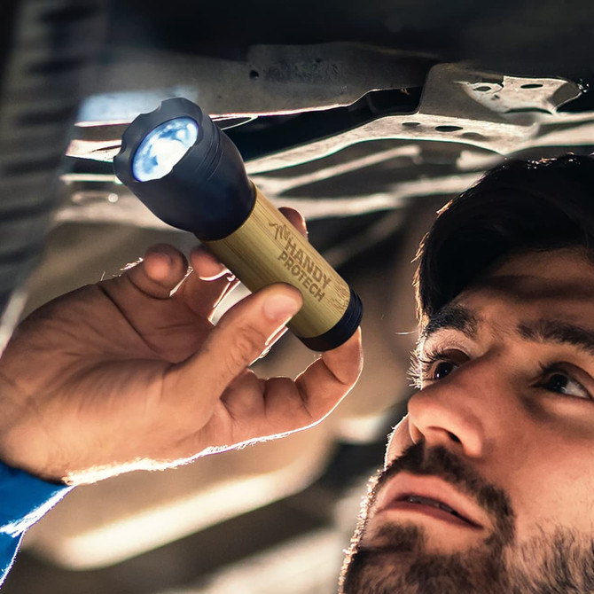 A bamboo torch with a black top is being held by a person looking underneath a vehicle.