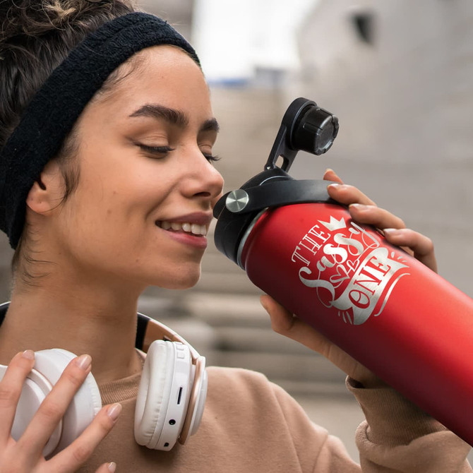 A drink bottle in gradient red with a black lid, featuring a logo. A person is holding it close to their face.