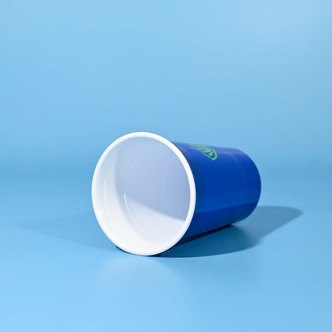 A drink cup with a blue exterior and white interior, featuring a logo, lying on a light blue background.