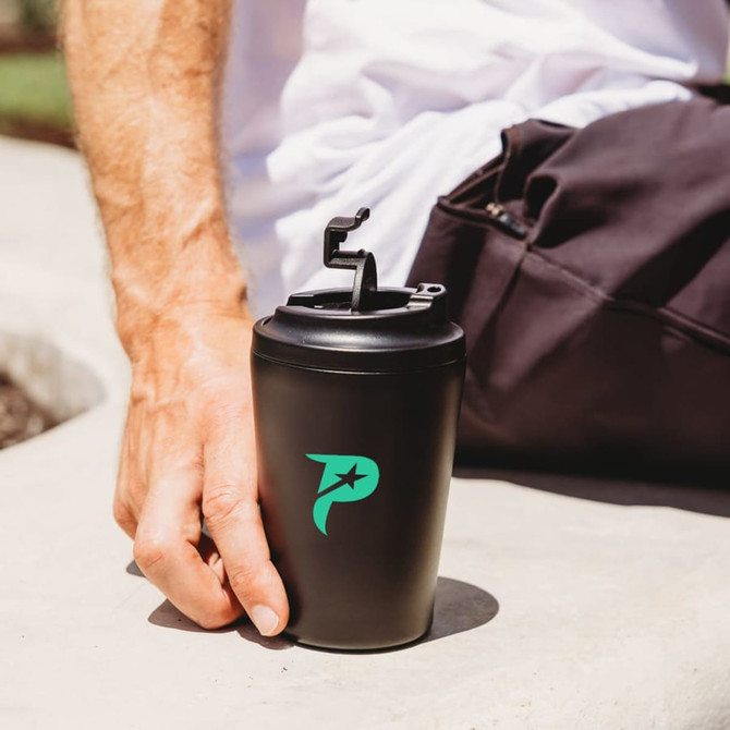 A travel cup in matte black with a green logo, featuring a secure lid and hand-held against a light background.