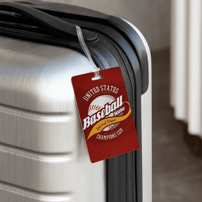 A red imprinted mini luggage tag is attached to a sleek, silver suitcase, featuring a logo and design.