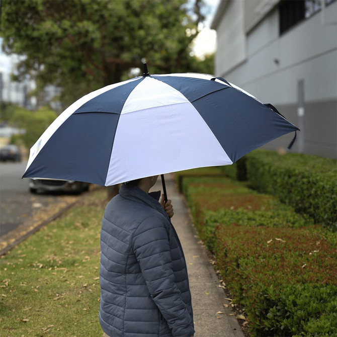 A recycled golf umbrella in navy blue and white, held by a person, with greenery in the background.
