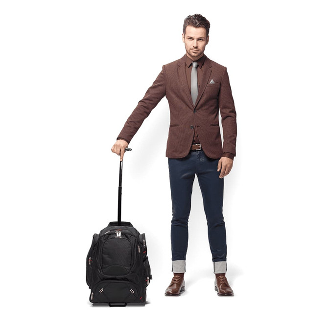 A man in a suit stands beside a black wheeled compu-backpack with a retractable handle.