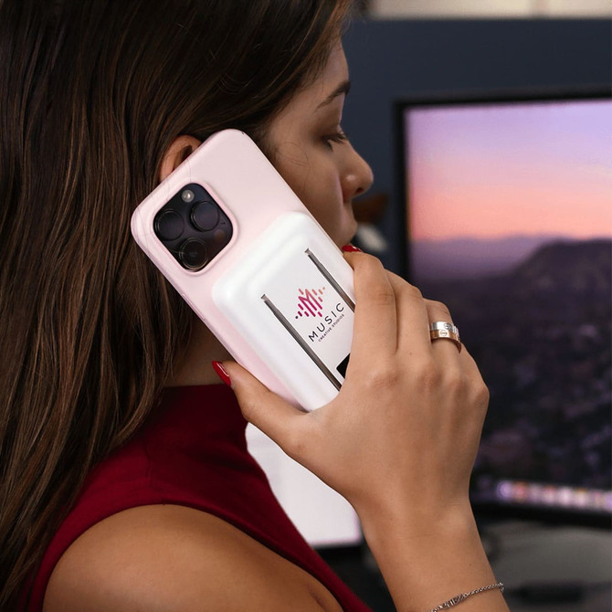 A pink magnetic power bank with a phone stand, held by a person near a computer screen. The product has a logo on it.