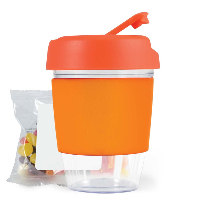 A reusable coffee cup with an orange lid and silicone sleeve, accompanied by a pack of jelly beans.